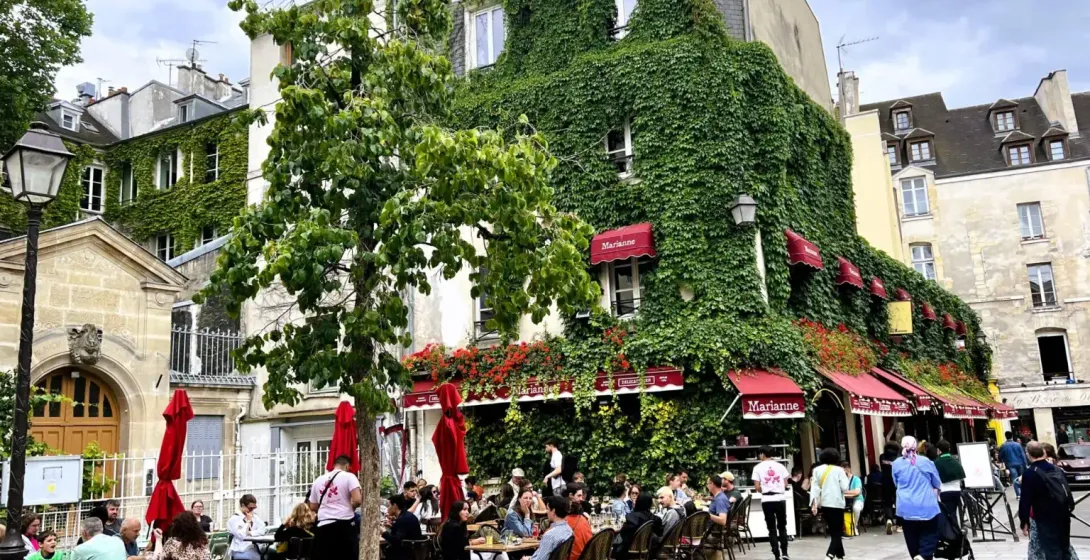Charming Parisian square with a restaurant named Marianne, surrounded by people enjoying outdoor dining.