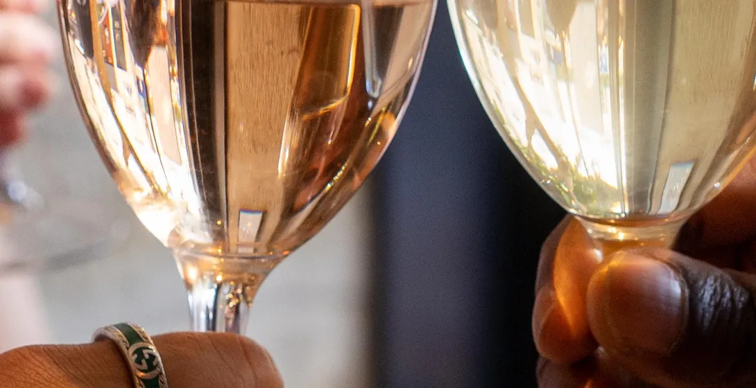 Close-up of three people's hands raising wine glasses with white and rosé wine for a toast.
