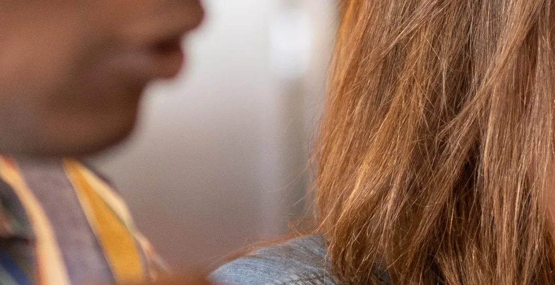 Close-up of two people, one with dark skin and the other with brown hair, in conversation indoors.