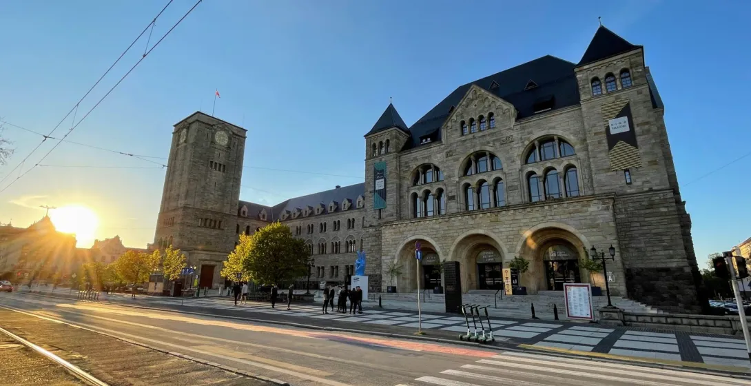Edificio de piedra del Castillo Imperial en Poznań con torre del reloj, vías de tranvía y paso de peatones. Sol bajo a la ...