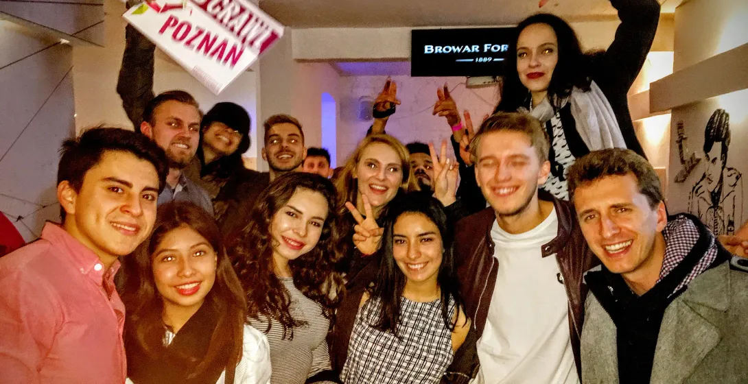 Group of smiling young adults holding a "Pub Crawl Poznan" sign indoors, with a "Browar Fortuna" sign in the background.