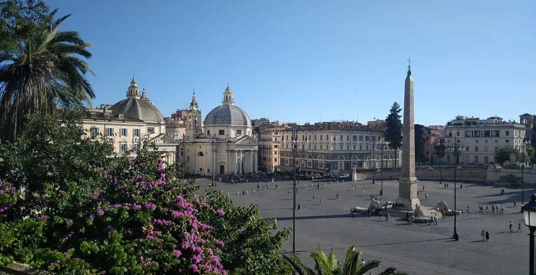 Elevated view of Piazza del Popolo in Rome showing the Flaminio Obelisk, twin churches, and people walking in the square.