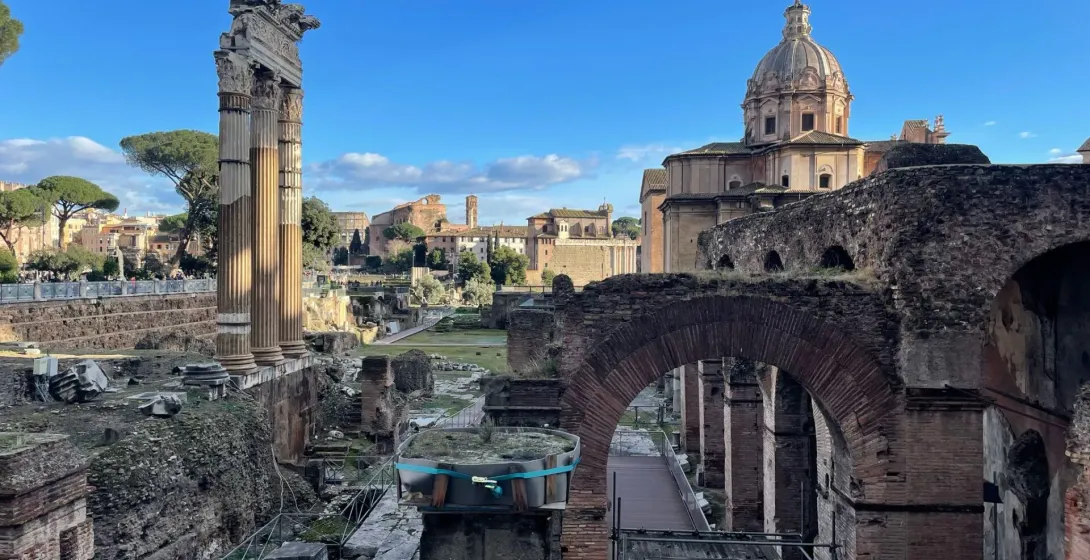 Ruinen des Forum Romanum mit Säulen des Saturn-Tempels, weiteren Tempeln und Besuchern unter blauem Himmel.