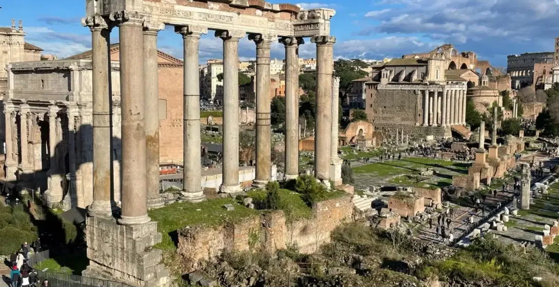 Vista del Foro Romano en Roma, mostrando ruinas antiguas, incluyendo ocho altas columnas del Templo de Saturno bajo un cie...