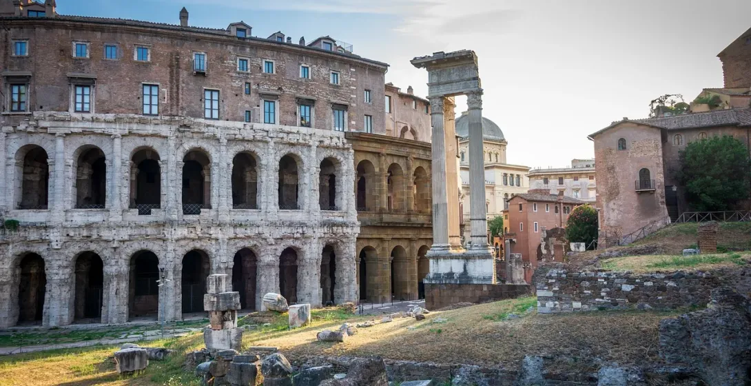 Ruiny starożytnego Teatru Marcellusa z łukową fasadą, nowoczesnymi budynkami u góry, rzymskimi kolumnami i gruzem na pierw...