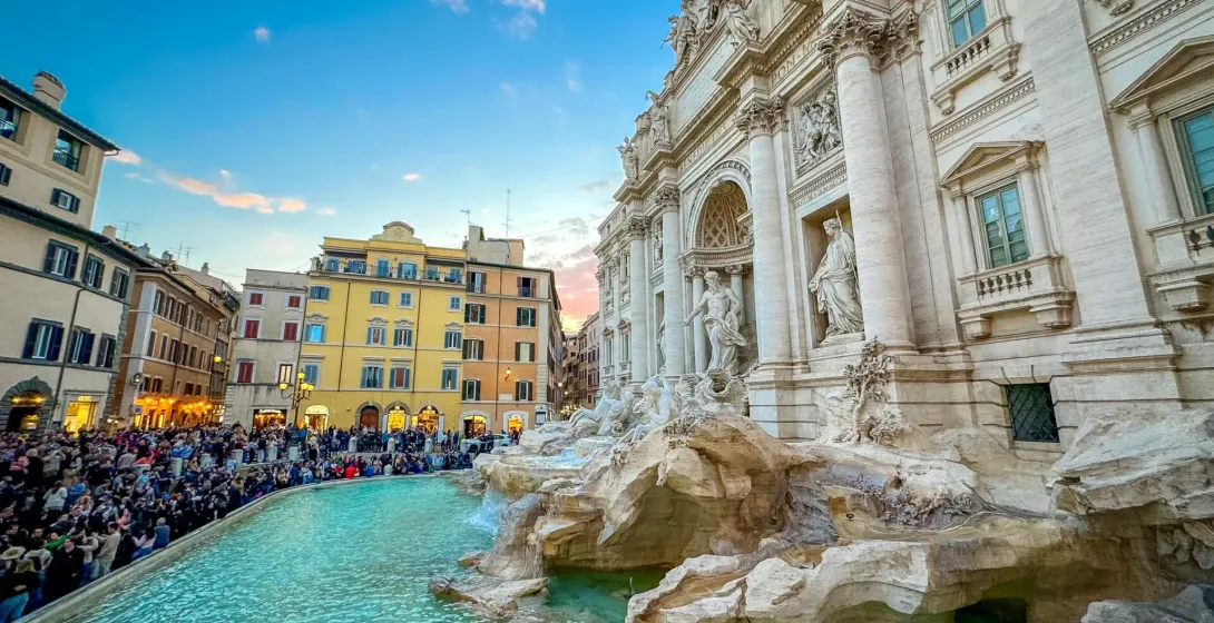 Abarrotada Fontana di Trevi en Roma al atardecer, con esculturas barrocas, agua turquesa y edificios históricos bajo un ci...