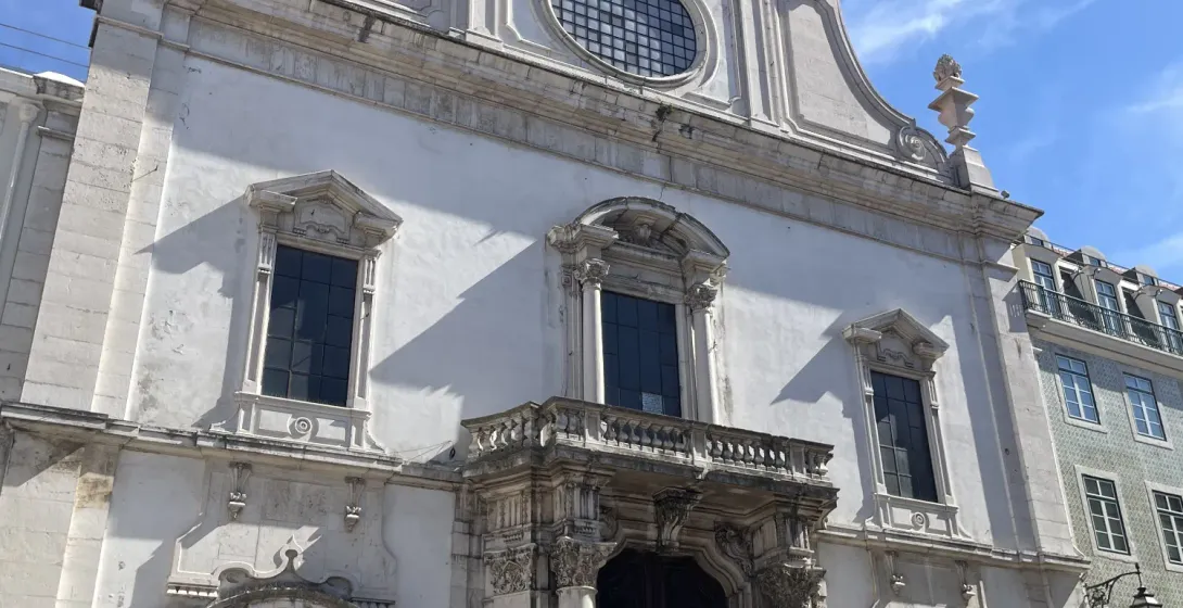 Fachada blanca de la iglesia de Sao Domingos en Lisboa con turistas reunidos cerca de la entrada en un dia soleado.