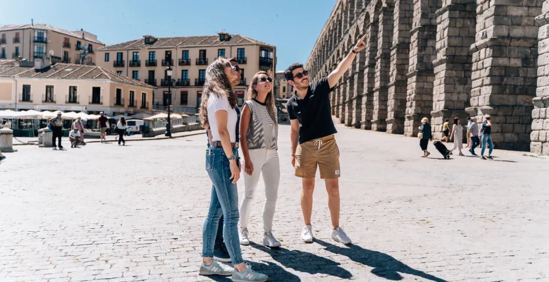 Un guía turístico señala el Acueducto de Segovia a tres turistas en un día soleado.