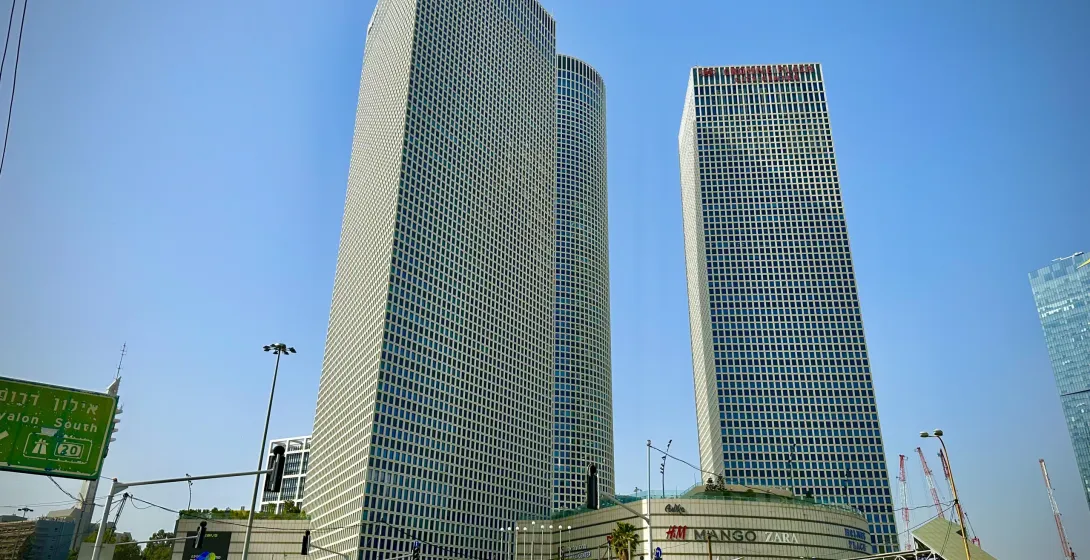 Modern skyscrapers of Azrieli Center dominate the skyline in Tel Aviv, with a busy street, pedestrians, and cars below on ...
