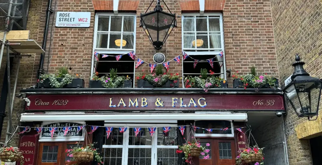La fachada de ladrillo del histórico pub Lamb & Flag en un estrecho callejón de Londres, decorada con flores y banderas br...