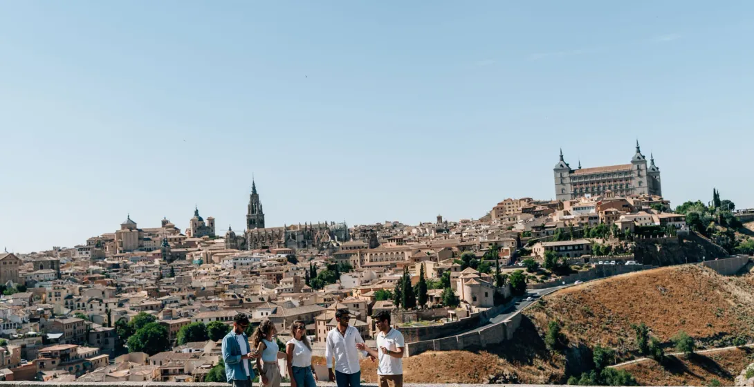 Un grupo de personas en un mirador con vistas a la histórica ciudad de Toledo, España, en un día soleado.