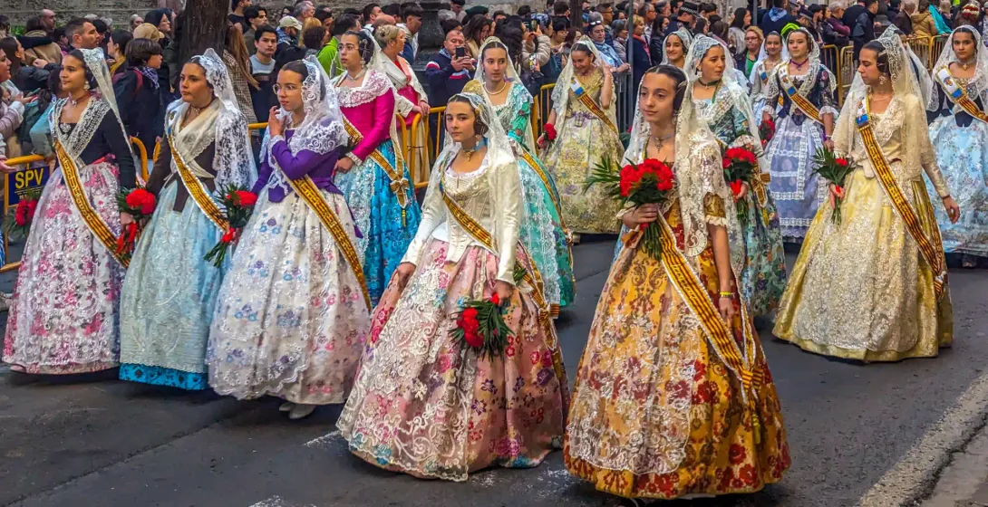 Un grupo de mujeres y niñas con coloridos y tradicionales trajes de fallera durante un desfile en Valencia.