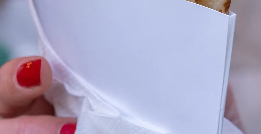 Close-up of a person's hands with red nail polish holding a sweet folded crepe wrapped in white paper.