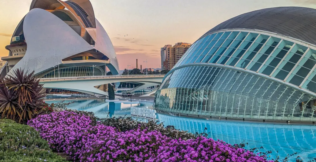 The modern buildings of the City of Arts and Sciences in Valencia at sunset, surrounded by water and flowers.