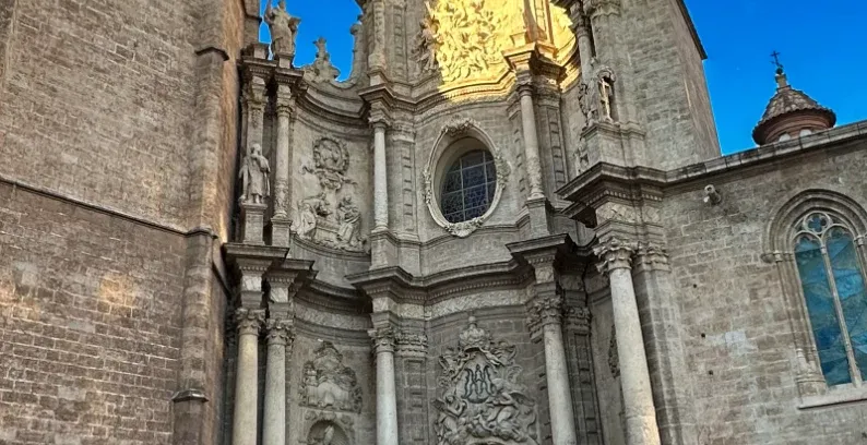 Baroque facade and bell tower of Valencia Cathedral under a clear blue sky, illuminated by sunlight.