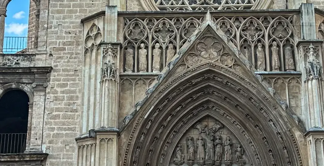 Close-up of Valencia Cathedral's Gothic facade, showing a rose window, detailed carvings, wooden doors, and a gargoyle.