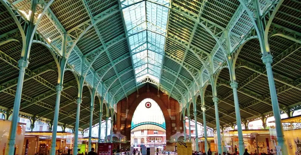 High vaulted ceiling with green metal trusses and a glass roof inside the Colón Market hall in Valencia.