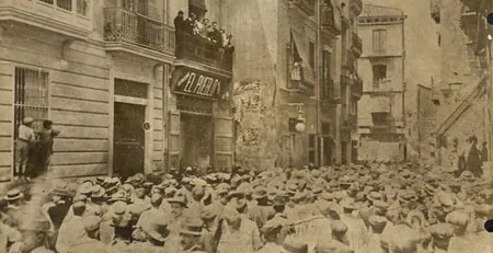 Historic, sepia-toned photo of a crowd gathered on a street in Valencia, in front of the 'El Pueblo' newspaper building.