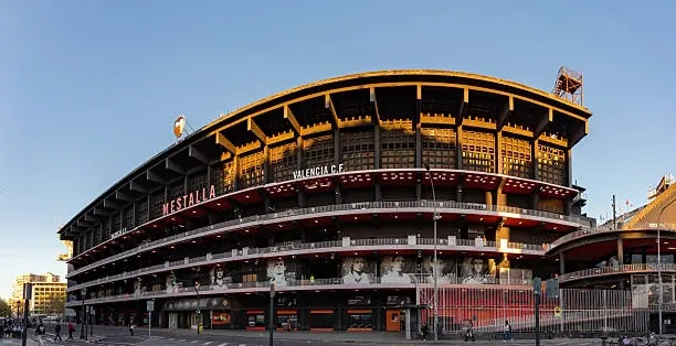 The curved exterior of Mestalla Stadium in Valencia, seen from a street corner during the golden hour.