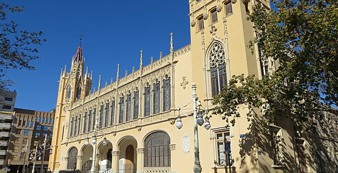 The ornate, neo-Gothic facade of the Palacio de la Exposición in Valencia on a sunny day, with cars parked out front.