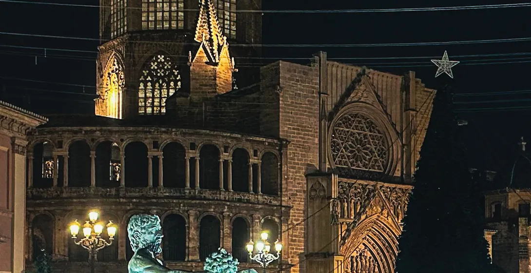 Illuminated Turia Fountain with bronze statues and the illuminated Valencia Cathedral at night. A large Christmas tree is ...