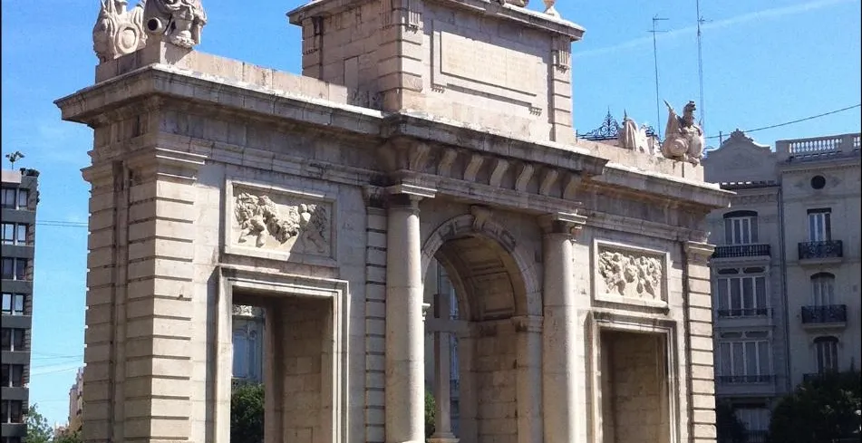 The Puerta del Mar triumphal arch in Valencia on a sunny day, with a bed of red flowers in the foreground.