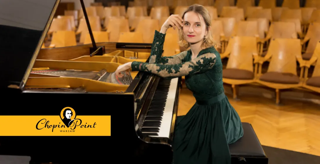 Woman in a green dress sitting at a grand piano in an empty concert hall.