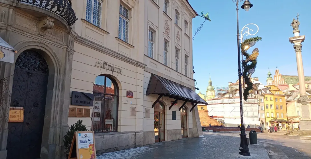 Facade of Dom Literatury (House of Literature) and buildings in Warsaw's Old Town, with a Chopin concert sign. Snowy pavem...