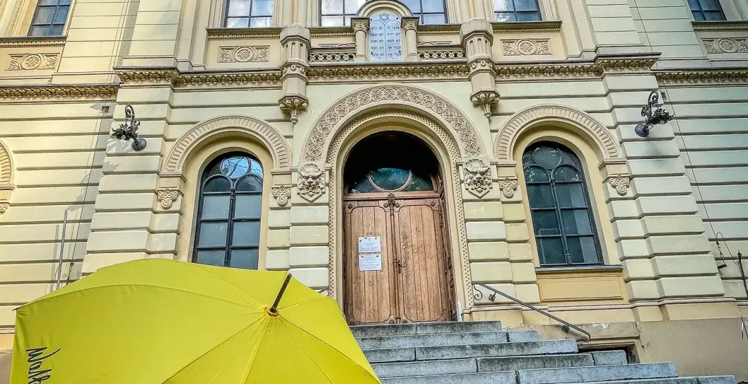 Front facade of the ornate Nożyk Synagogue in Warsaw, a yellow Walkative umbrella on stone steps in the foreground.