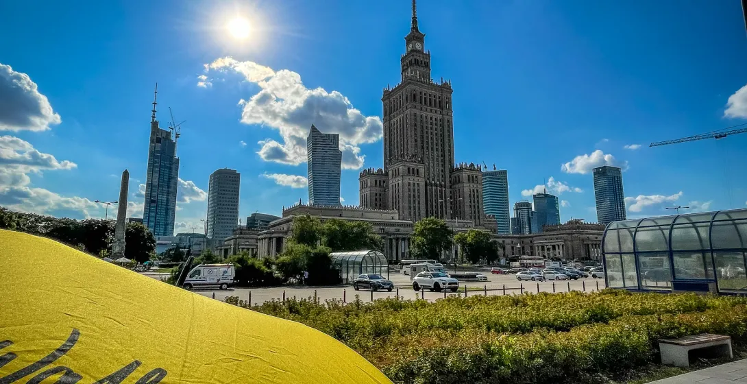 Palace of Culture and Science and modern skyscrapers under a sunny blue sky, with a yellow Walkative umbrella in the foreg...