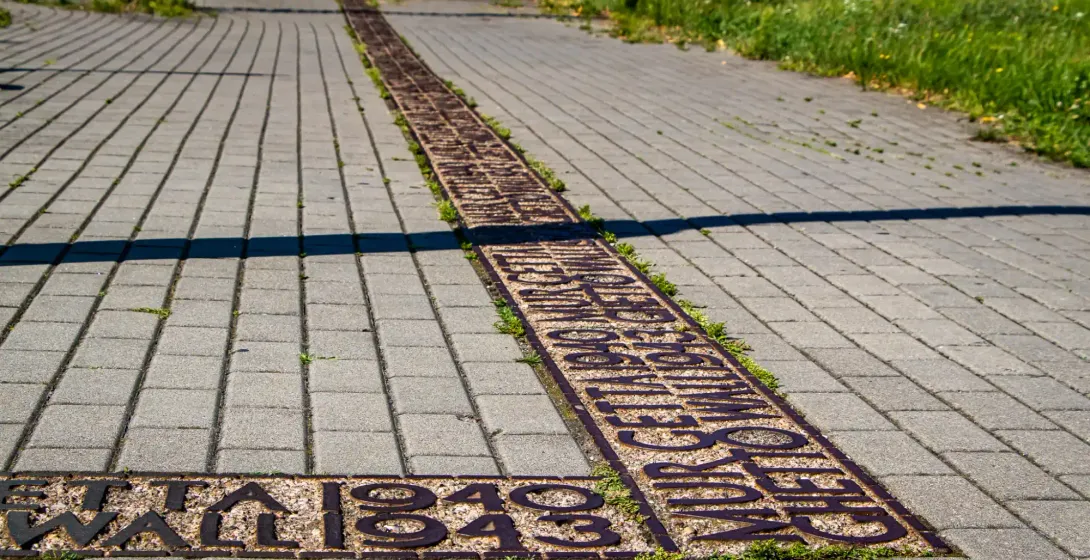 Metal inlay in light gray pavement marking the former Warsaw Ghetto boundary with text 'GETTO WARSZAWSKIE 1940 1943'.