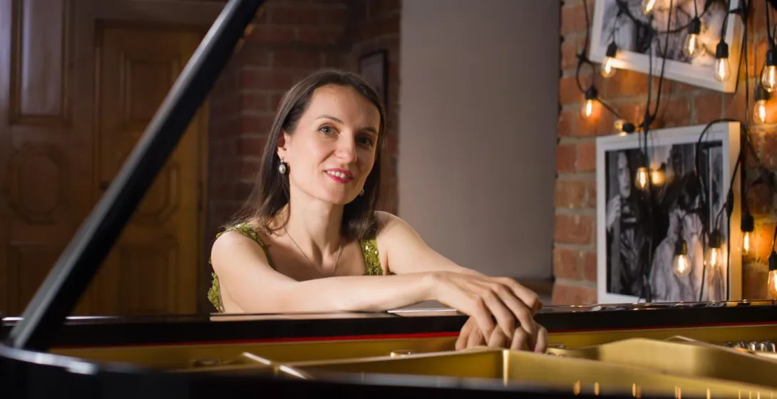 La pianista Aleksandra Hurkała se apoya en un piano de cola en una sala con paredes de ladrillo.