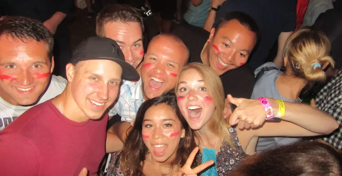 Junge Leute mit roter Gesichtsfarbe auf den Wangen lächeln, posieren eng zusammen bei einem lebhaften Event. Armbänder sic...