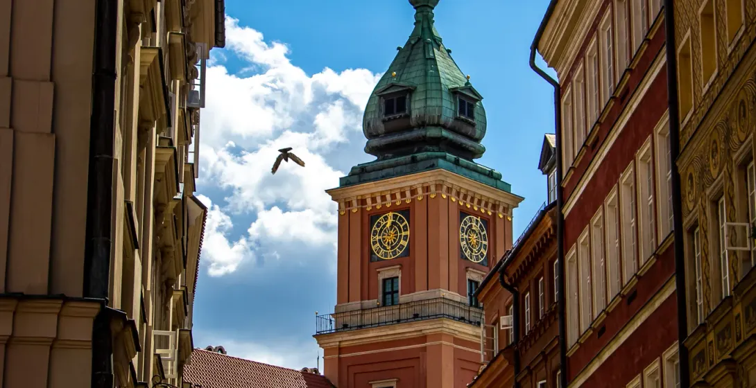 Vista de una calle estrecha hacia la torre del reloj del Castillo Real de Varsovia con cúpula verde, esferas doradas y un ...