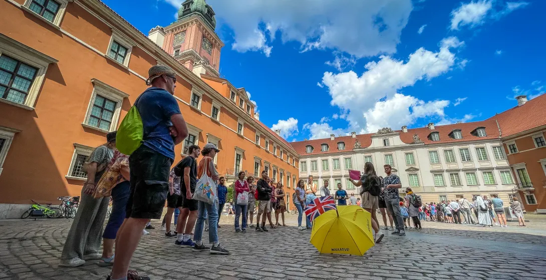 Grupo turístico con guía y paraguas amarillo en un patio adoquinado frente al Castillo Real de Varsovia.