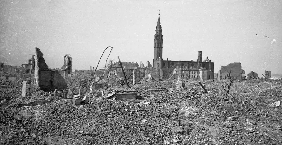 Foto en blanco y negro de una ciudad devastada por la guerra, con un vasto campo de escombros en primer plano y una iglesi...