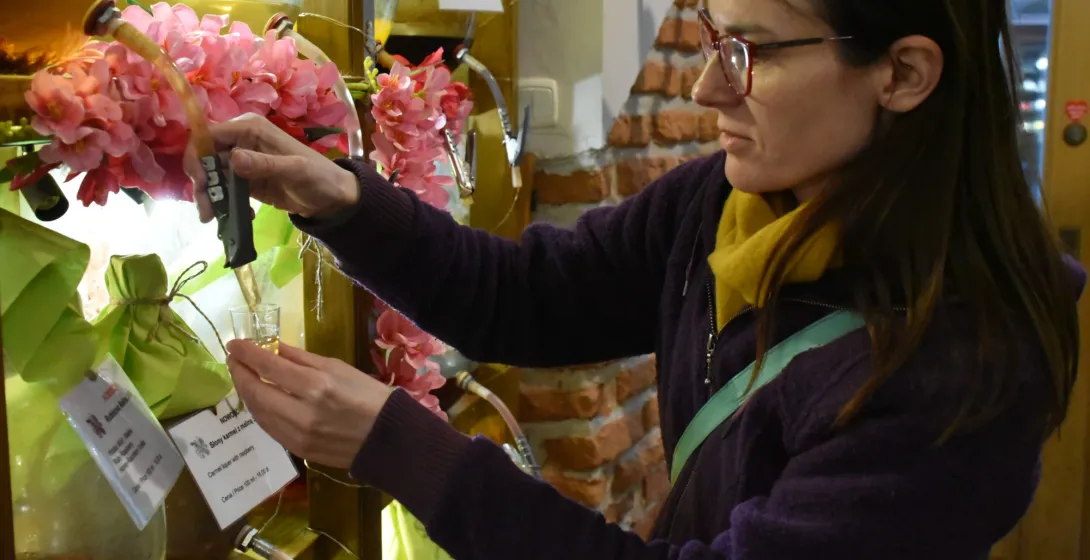 Woman pouring traditional Polish liqueur from a glass dispenser into a tasting glass in a Krakow shop.