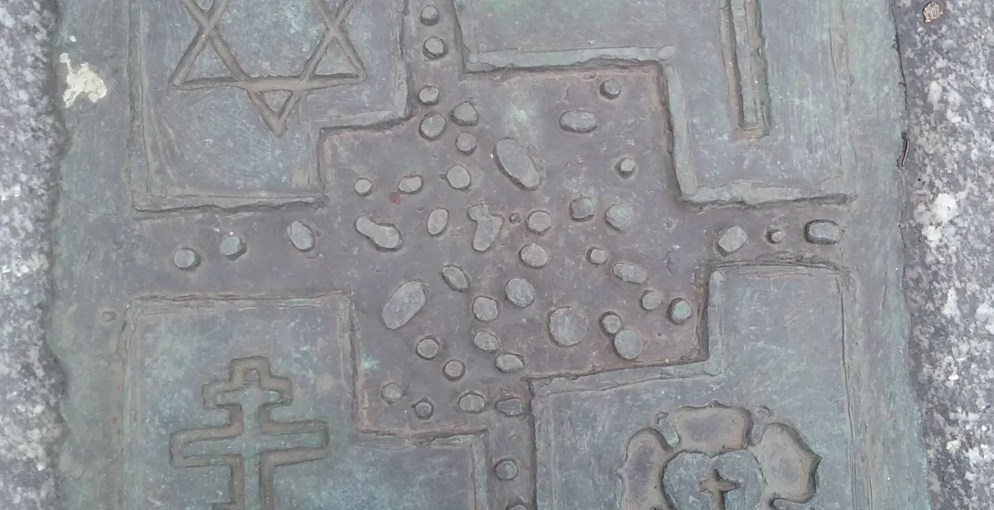 Brązowa tablica w granicie z czterema symbolami religijnymi: Gwiazda Dawida, krzyż łaciński, krzyż prawosławny i róża Lutra.