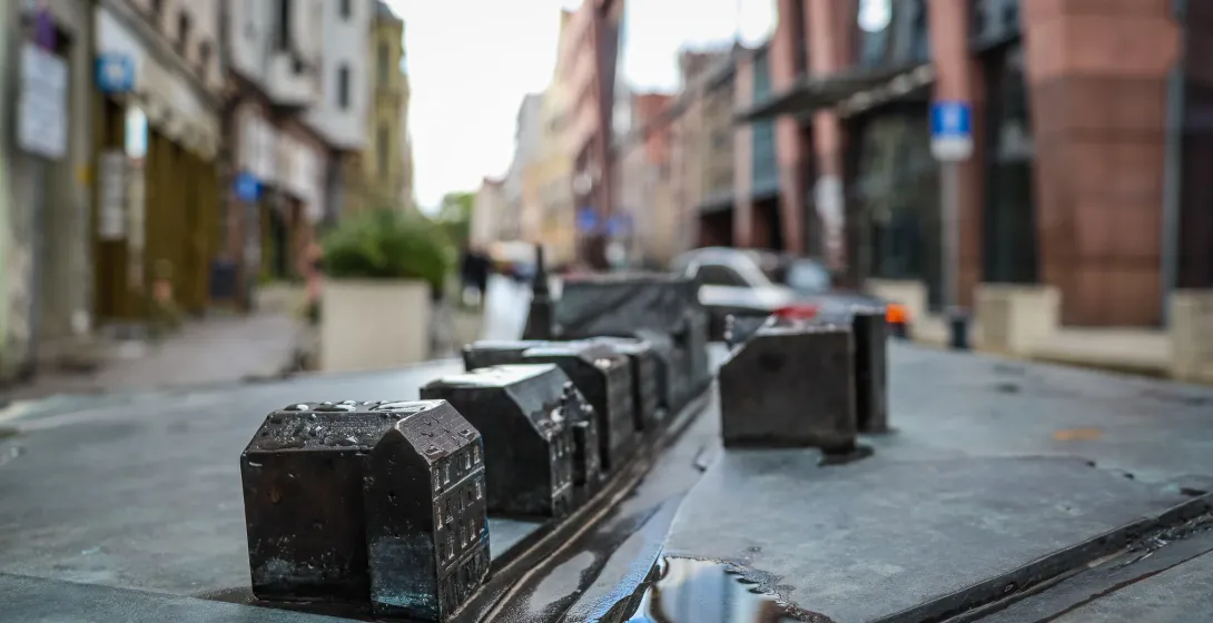 Zbliżenie na ciemny, metalowy model miniaturowych budynków miejskich z kałużami wody, z rozmytym tłem prawdziwej ulicy.