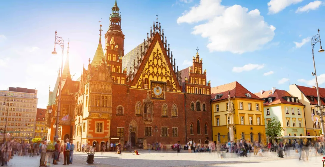 Wroclaw Old Town Hall and colorful surrounding buildings on Market Square, with blurred tourists and bright sunlight.