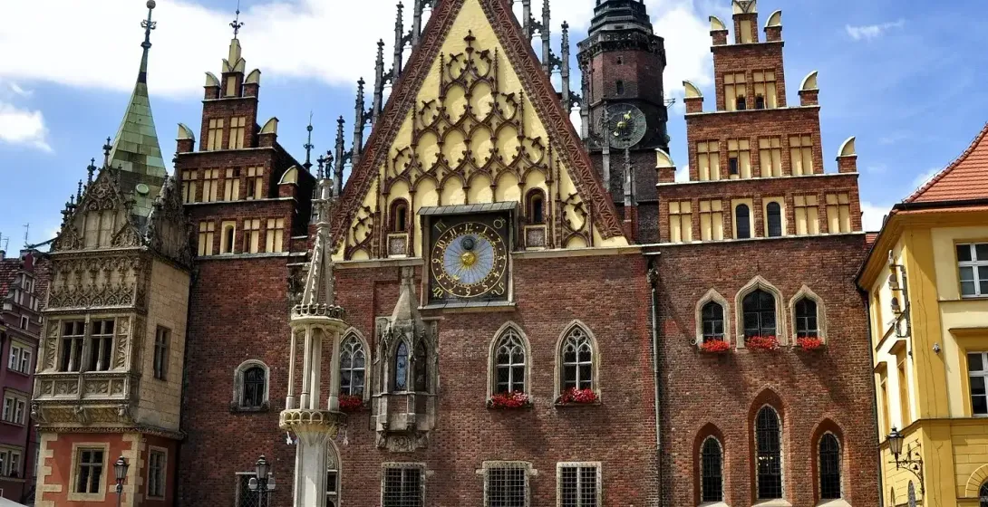 Gotycki ceglany Ratusz we Wrocławiu z dużym zegarem, ozdobnymi szczytami i wysoką wieżą. Ludzie gromadzą się na brukowanym...