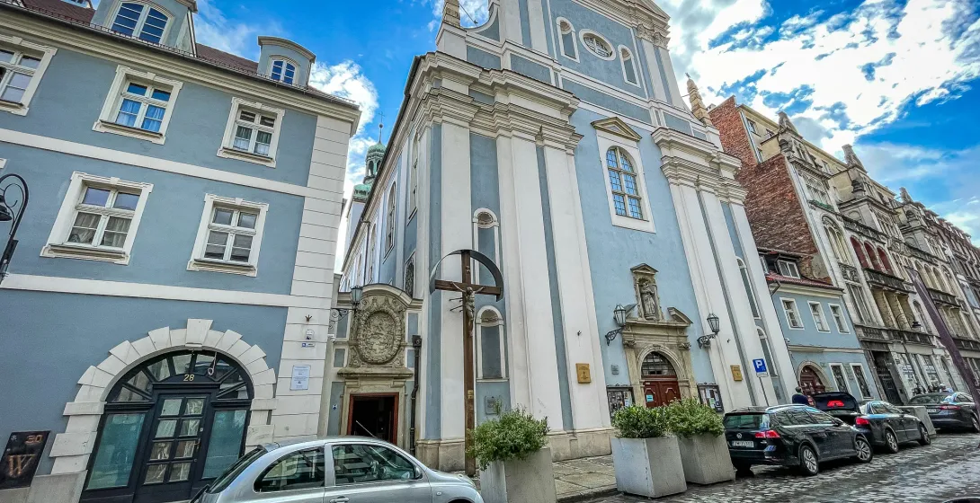 Jasnoniebieska barokowa fasada kościoła św. Antoniego z Padwy przy brukowanej ulicy we Wrocławiu pod błękitnym niebem.