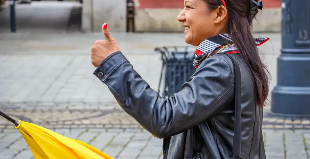 A female tour guide with a yellow Walkative umbrella gives a thumbs-up on a cobblestone street in Wroclaw.