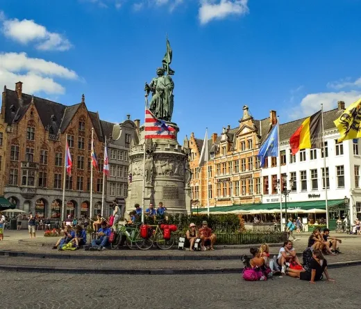 Turyści cieszą się rynkiem w Brugii, Belgia, ze statuetką Jana van Eycka w tle.