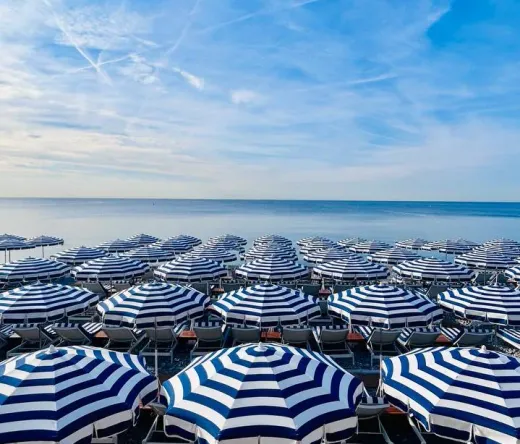 Reihen von blau-weiß gestreiften Sonnenschirmen und Liegestühlen an einem Strand in Nizza.