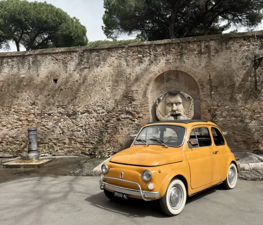 Un Fiat 500 amarillo aparcado cerca de una muralla romana con una fuente única.