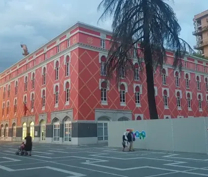 Turyści zwiedzający żywo różowy budynek i wieżę zegarową w Tiranie, Albania.