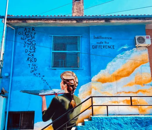 Kolorowy mural przedstawiający kobietę z książką na niebieskim budynku.