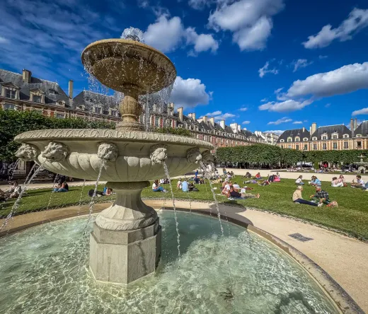 Una pintoresca fuente en la Place des Vosges, Le Marais, París, rodeada de gente disfrutando de un día soleado.