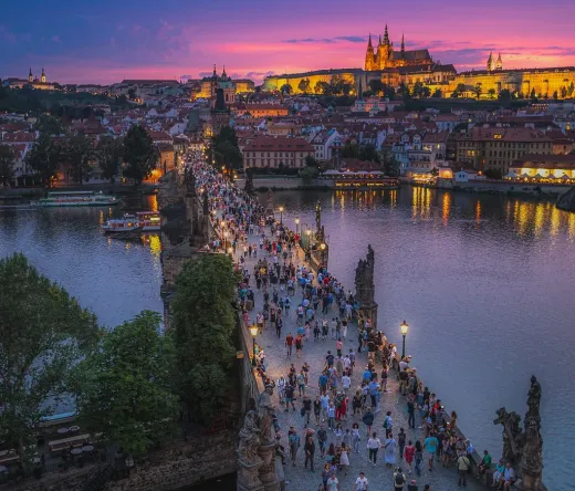 Touristen schlendern bei Sonnenuntergang über die Karlsbrücke in Prag, im Hintergrund thront majestätisch die Prager Burg.